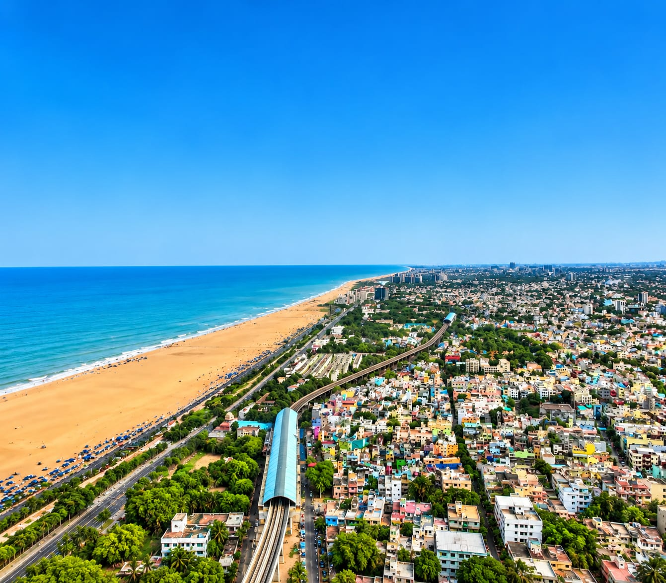 Aerial view of a coastal city, beachfront, and railway under a blue sky.